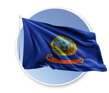 The state flag of Idaho blowing in the wind. The flag is dark blue with the Idaho state seal and the words State of Idaho.